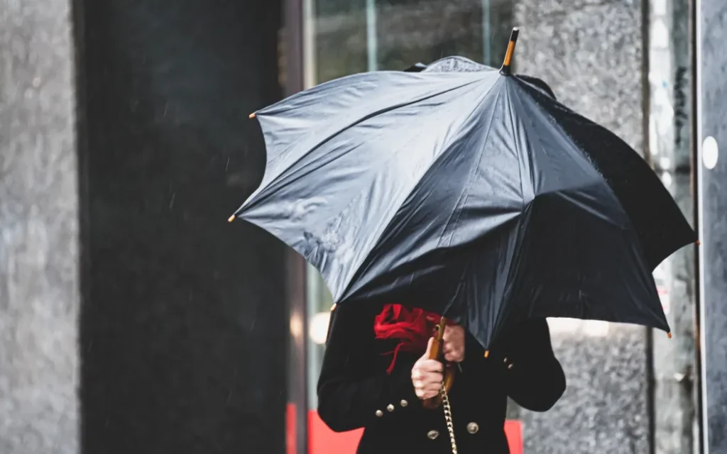 A woman has difficulty holding an umbrella from strong winds in rainy weather.