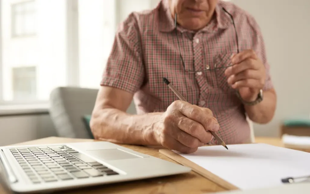 Closeup portrait of unrecognizable senior man filling in papers while working with laptop at home