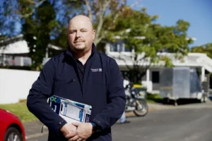 Compliance Manager Adrian Wilson stands in the middle of a street holding documents.