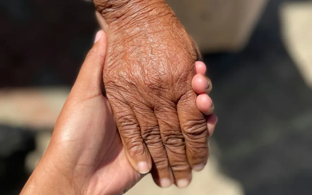 A person offers support, holding the hand of an elderly person.