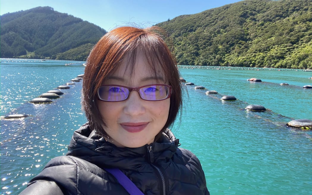 Professor Bing Xue of Victoria University of Wellington, with a mussel farm visible in the water in the background.