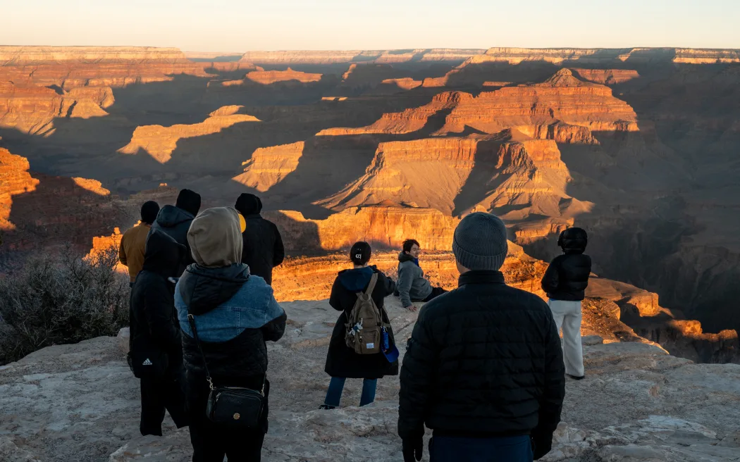 Chính phủ Mỹ đóng cửa: Du khách cần biết gì khi đến xứ cờ hoa? 3 GRAND CANYON, ARIZONA - FEBRUARY 22: Tourists overlook the Grand Canyon at sunrise on February 22, 2025 in Grand Canyon, Arizona. The Trump administration is planning to restore jobs for dozens of National Park Service employees after laying off approximately 1,000 probationary employees amid a wave of federal work force cuts. In addition, the Trump administration has pledged to restore 50 jobs along with the hiring of an additional 3,000 seasonal workers. Brandon Bell/Getty Images/AFP (Photo by Brandon Bell / GETTY IMAGES NORTH AMERICA / Getty Images via AFP)