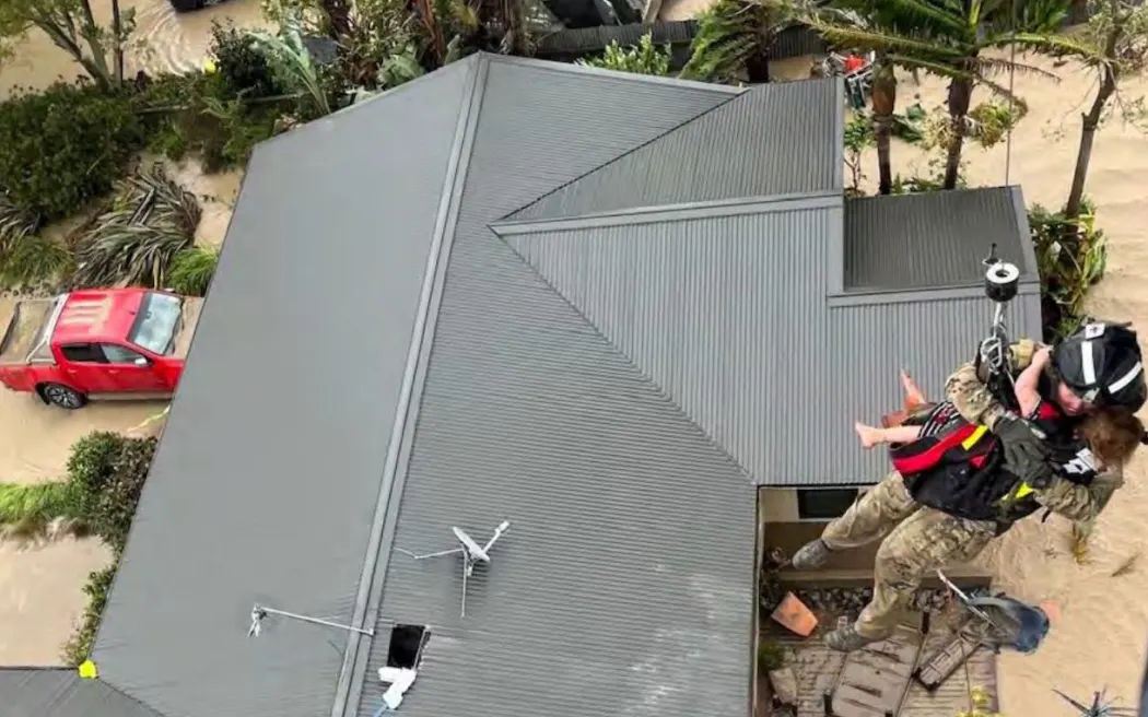 Imogen Collins is lifted to safety from the rooftop her family climbed onto to escape the floodwaters on North Shore Road.