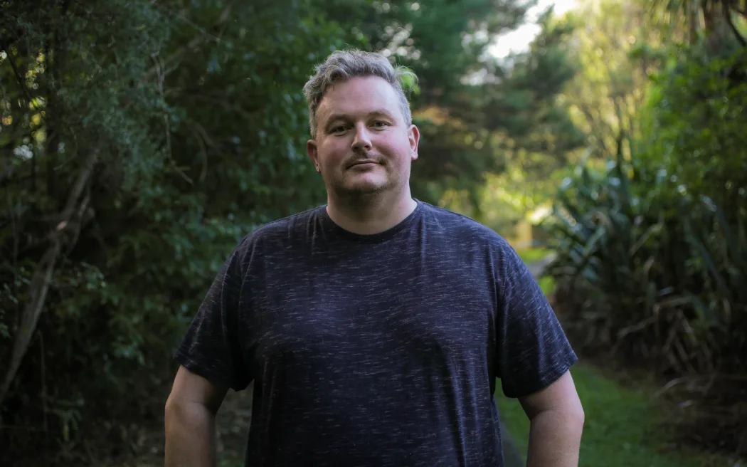 Hạn chót mua lại nhà ngập lụt cận kề: 16 chủ nhà Auckland vẫn bất đồng với chính quyền 5 Lyall Carter, a tall man with curly blond hair, stands on a narrow footpath amid bush near his home in West Auckland.