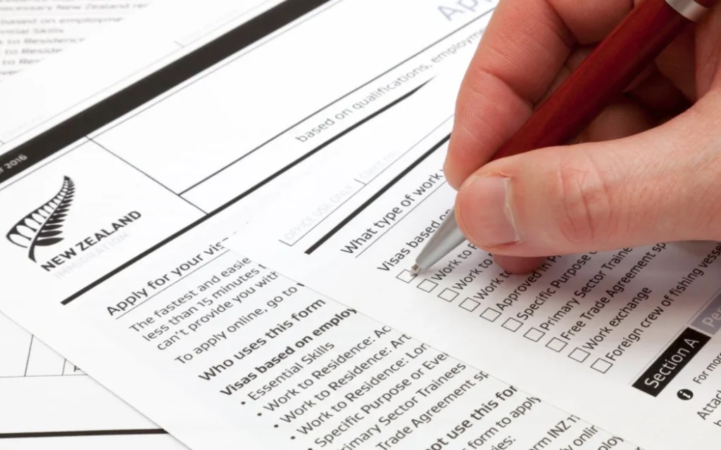 A man holding a ballpoint pen to fill a work visa application form to New Zealand.