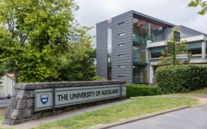 Auckland, New Zealand - March 1, 2017: Sign and logo of University of Auckland set near modern dark gray offices in green park like environment.