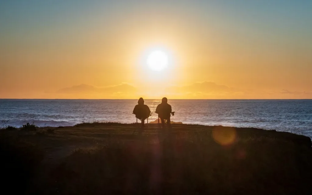Chênh lệch tuổi tác trong tình yêu: Tiền bạc có bị ảnh hưởng? 1 A couple sit together on fold out chairs watching a sunset over the sea.