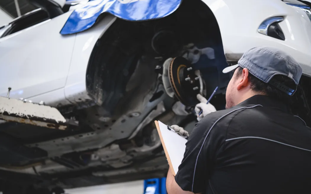 Asian male car technician car maintenance for customers according to specified vehicle maintenance checklist. Disk brake pad wear automotive repairing on vehicle. Safety inspection check service