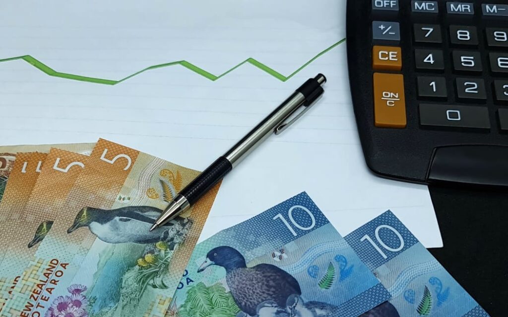 WorkSafe cắt giảm 1/3 đội ngũ chuyên trách rủi ro tâm lý xã hội: Nguy cơ bỏ ngỏ sức khỏe tinh thần người lao động? 1 New Zealand banknotes, pen and calculator on background with rising trend green line. Money finance economy