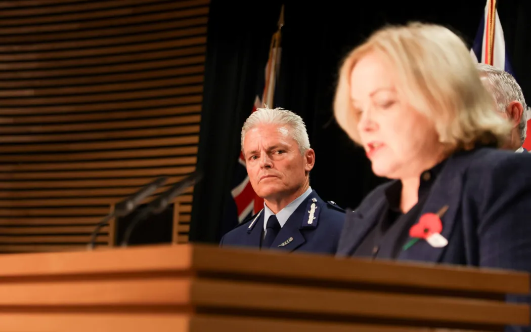 Public Services Minister Judith Collins speaks after a damning report into police conduct, with Police Commissioner Richard Chambers in the background.